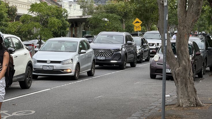 Traffic queued southbound on Wellington Street, Clifton Hill, during morning peak, with the St John's Anglican Church spire visible in the background